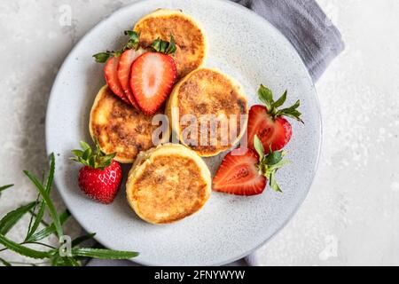 Frittelle o frittelle di formaggio cottage con fragola e yogurt naturale su sfondo grigio chiaro. Colazione o pranzo sani. Syrniki. Vista dall'alto. Foto Stock