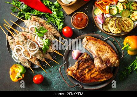 Kebab Kofta fatti in casa, bistecca alla griglia e verdure alla griglia su uno spiedino con verdure e salsa di pomodoro su un piano di pietra scuro. Vista dall'alto, disposizione piatta b Foto Stock