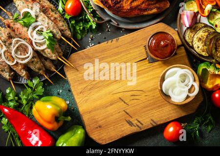 Kebab Kofta fatti in casa, bistecca alla griglia e verdure alla griglia su uno spiedino con verdure e salsa di pomodoro su un piano di pietra scuro. Vista dall'alto, disposizione piatta b Foto Stock