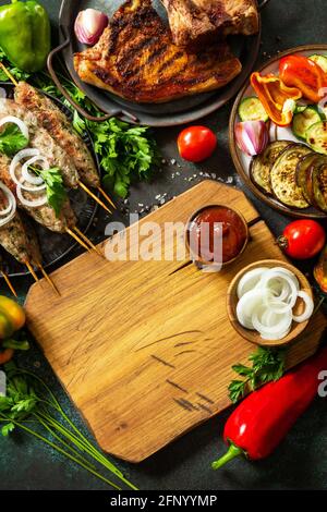 Kebab Kofta fatti in casa, bistecca alla griglia e verdure alla griglia su uno spiedino con verdure e salsa di pomodoro su un piano di pietra scuro. Vista dall'alto, disposizione piatta b Foto Stock
