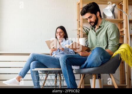 Trascorrere del tempo a casa. Accoppia l'uno con l'altro e sorridendo durante la lettura di libro, tablet Foto Stock