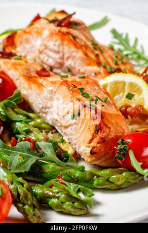 filetti di salmone alla griglia con limone e pancetta caramellate serviti con asparagi, pomodori, insalata di razzi selvatici, vista verticale, primo piano Foto Stock