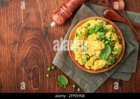 Purè di patate con burro, piselli verdi, cipolle, basilico su un rustico sfondo di legno. Vista dall'alto con primo piano. Foto Stock