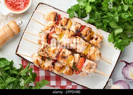 Kebab di pollo o spiedini kebab in piastra di ceramica, spezie, erbe di coriandolo e verdure su sfondo bianco del tavolo. Barbecue ingredienti crudi per g Foto Stock