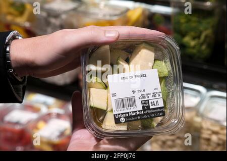 Mani di donna che tengono un contenitore trasparente di plastica di zucchine appena tagliate, mostrando etichetta prodotto con descrizione e prezzo, Williamsburg, New York Foto Stock