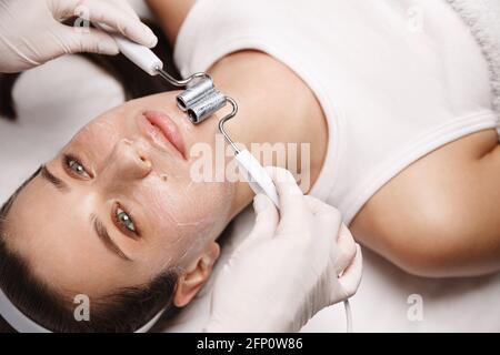 Donna in clinica di bellezza che giace sul tavolo di terapia, estetista in guanti usa gel galvanico e macchina elettronica per aumentare l'ossigeno nelle cellule del viso, ringiovanire Foto Stock