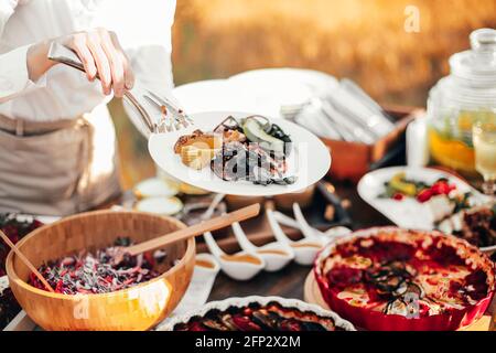 Alto angolo di raccolto anonimo persona con pinze che prendono pezzo di formaggio da vassoio posto su tavolo a buffet durante l'esterno evento Foto Stock