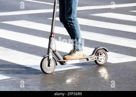 Belgrado, Serbia - 13 maggio 2021: Primo piano di gambe in sella a uno scooter elettrico mentre si attraversa la strada bagnata in una giornata luminosa e soleggiata e piovosa Foto Stock