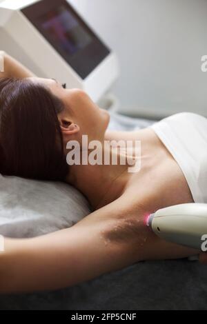 Dall'alto della cliente femminile sdraiata sul divano in bellezza salone durante l'epilazione laser delle ascelle Foto Stock