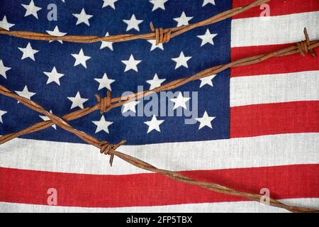 Primo piano di recinzioni arrugginite di filo spinato sulla bandiera americana Foto Stock