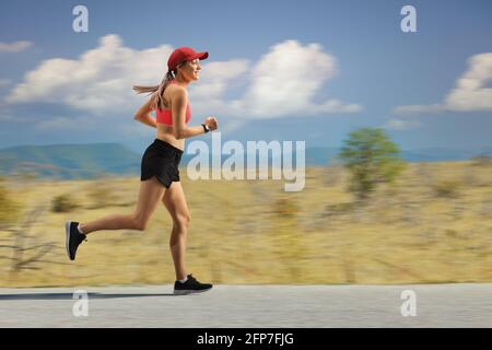 Donna che corre in periferia su una strada asfaltata Foto Stock