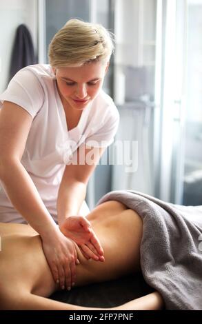 Master senza volto che dà massaggio di muscoli della schiena e delle spalle a. donna anonima sdraiata sul tavolo nel salone termale Foto Stock