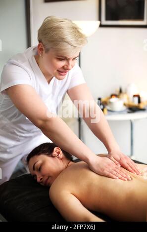 Master senza volto che dà massaggio di muscoli della schiena e delle spalle a. donna anonima sdraiata sul tavolo nel salone termale Foto Stock