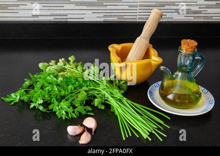 Cottura di Malta, prezzemolo, aglio e olio d'oliva su una panca di granito nero con una parete di piastrelle a strisce grigie. Foto Stock