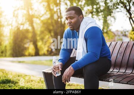 Uomo esausto dopo l'esercizio di acqua potabile mentre si siede su panca. Foto Stock