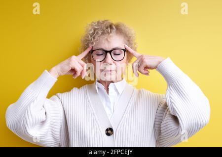 donna caucasica anziana che guarda stressata e frustrata, lavorando sotto pressione con mal di testa e turbato con problemi, tenendo le dita sulle tempie Foto Stock
