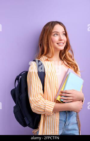 Giovane studente biondo gioisce a nuove lezioni, femmina eccitato circa seminario di formazione isolato su sfondo viola brillante, guardando al lato con sognante f Foto Stock