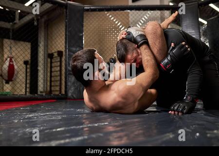 Grappler cercando di soffocare l'avversario in lotta a terra, allenamento in palestra. Due uomini atletici impegnati in mma, pugilato, lotta senza regole Foto Stock