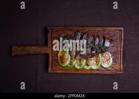 agnello arrosto con zucchine su tavola di legno. Foto Stock