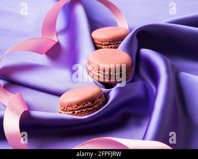 Amaretti francesi rosa pastello su fondo di tessuto di seta viola Foto Stock