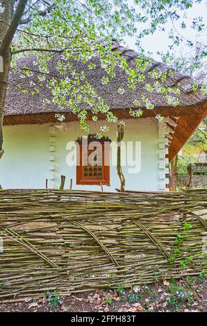 La casa di hata imbiancata con finestra di legno e recinzione di paglia dietro il tyn (recinzione di vimini), Mamajeva Sloboda Cossack Village scansen, Kyiv, Ukrain Foto Stock