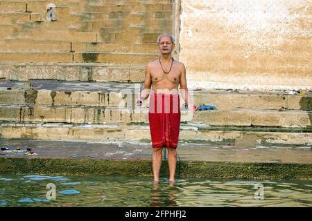 Varanasi, India - 01 novembre 2016: Un vecchio pellegrino indù che esegue rituali o preghiere in dhoti con diya o candela nella palma sul fiume gange in Foto Stock