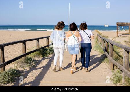 Tre donne che camminano attraverso un ponte sulla spiaggia Foto Stock