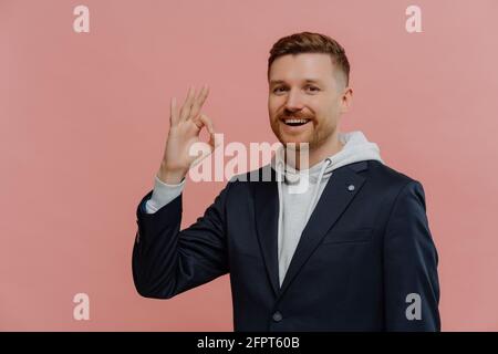 Felice uomo rosso che mostra un gesto OK isolato su parete rosa Foto Stock