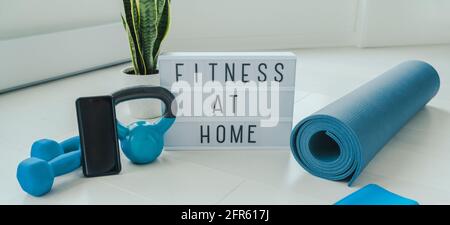 Fitness a casa lightbox segno in soggiorno per on-line allenati su un'app per telefono in interni con pesi a manubri e. bande di resistenza sul tappetino yoga Foto Stock