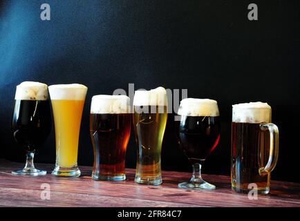 Sei bicchieri di diverse birre sono su un tavolo di legno contro una parete nera. Primo piano. Foto Stock