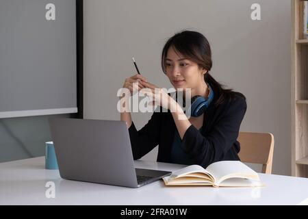 Una donna ascolta un webinar didattico sul suo laptop mentre indossa le cuffie. Foto Stock