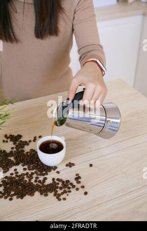 Donna in una cucina scandinava leggera versa il caffè da un macchina da caffè in tazza al mattino Foto Stock