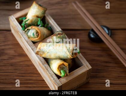 Cucina Asiatica. Primo piano del rotolo di molla servito in scatole decorative di legno con il chopstick. Involtini di primavera cinesi fritti con salsa di peperoncino dolce. Antipasti asiatici o spuntini. Foto Stock