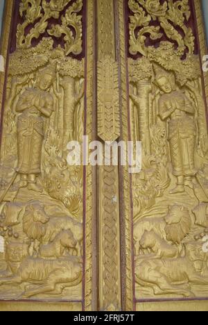 Porta decorativa con scultura in oro di figura religiosa nella foresta circondata da animali, Wat Hai Sok Tempio, Vientiane, Lao Foto Stock