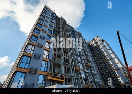 Edificio nuovo e moderno in costruzione contro il cielo blu. Costruttori che lavorano in basi di costruzione sospese sulla facciata. La gru è nelle vicinanze Foto Stock