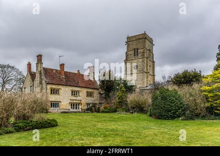 Manor Farm accanto alla chiesa di San Giovanni Evangelista nel villaggio di Wicken, Northamptonshire, Regno Unito; entrambi gli edifici risalgono al 17 ° secolo Foto Stock