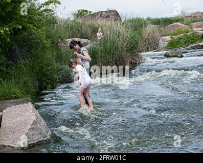 Cascate di Tokovsky, Ucraina - 05.16.2021: La gente sta attraversando un fiume che scorre velocemente. I turisti camminano sulle rocce in acque poco profonde. Foto Stock