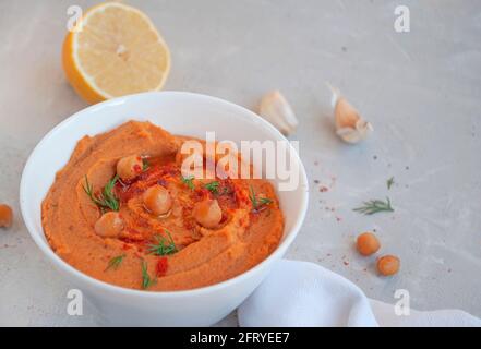 Una ciotola di delizioso hummus con olio d'oliva, aglio e paprika su sfondo grigio. Foto Stock