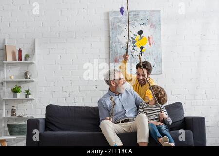 Ragazzo e uomo con canne da pesca giocattolo che guardano il nonno a casa Foto Stock