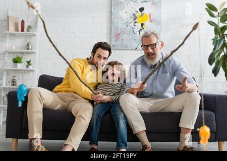 Ragazzo eccitato che gioca a pescare con padre e nonno a casa Foto Stock