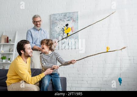 Padre e il figlio allegro che gioca a pesca giocattolo vicino nonno offuscato Foto Stock