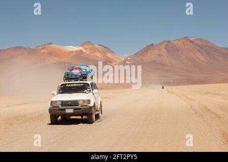 Sullo sfondo di vulcani, un veicolo fuoristrada 4x4 attraversa il paesaggio desertico della Bolivia in un safari turistico terrestre. Foto Stock