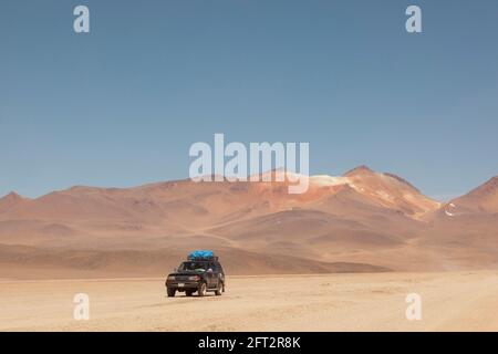 Sullo sfondo di vulcani, un veicolo fuoristrada 4x4 attraversa il paesaggio desertico della Bolivia in un safari turistico terrestre. Foto Stock