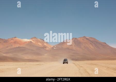 Sullo sfondo di vulcani, un veicolo fuoristrada 4x4 attraversa il paesaggio desertico della Bolivia in un safari turistico terrestre. Foto Stock