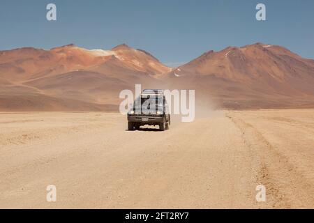 Sullo sfondo di vulcani, un veicolo fuoristrada 4x4 attraversa il paesaggio desertico della Bolivia in un safari turistico terrestre. Foto Stock