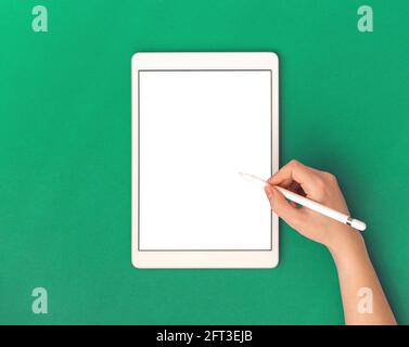Formazione sui tablet e mockup delle applicazioni con schermo bianco vuoto e mano della donna che utilizza la matita dello stilo, sfondo verde dell'area di lavoro dell'ufficio, vista dall'alto e co Foto Stock