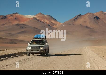 Sullo sfondo di vulcani, un veicolo fuoristrada 4x4 attraversa il paesaggio desertico della Bolivia in un safari turistico terrestre. Foto Stock