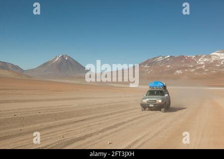 Sullo sfondo di vulcani, un veicolo fuoristrada 4x4 attraversa il paesaggio desertico della Bolivia in un safari turistico terrestre. Foto Stock