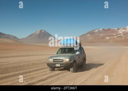 Sullo sfondo di vulcani, un veicolo fuoristrada 4x4 attraversa il paesaggio desertico della Bolivia in un safari turistico terrestre. Foto Stock