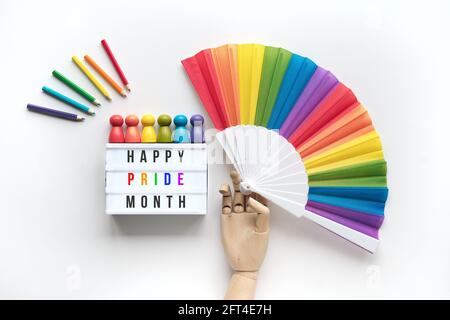 LGBTQ orgoglio mese decorazione. Text Happy Pride Month su lightbox. Oggetti con motivo arcobaleno su sfondo bianco spento. Il modello a mano in legno tiene la ventola arcobaleno. Legno Foto Stock